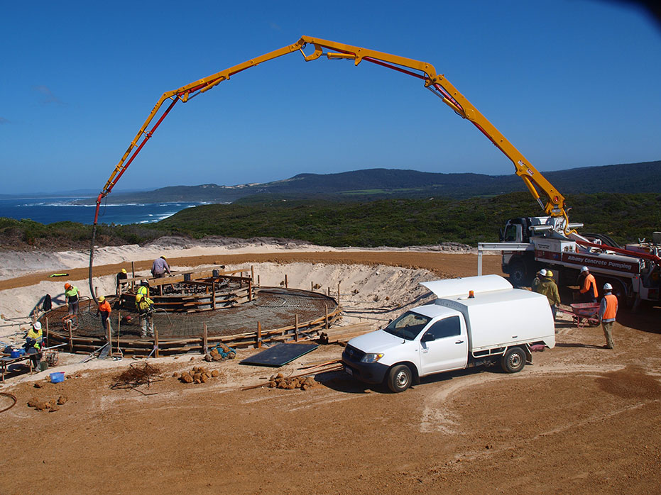 A photo of a concrete pumping truck with people helping pour the concrete for the footing.