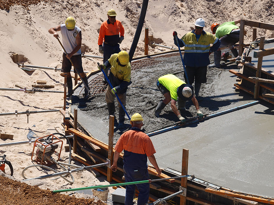 A photo of people screeding the concrete to make the top of the footing smooth.