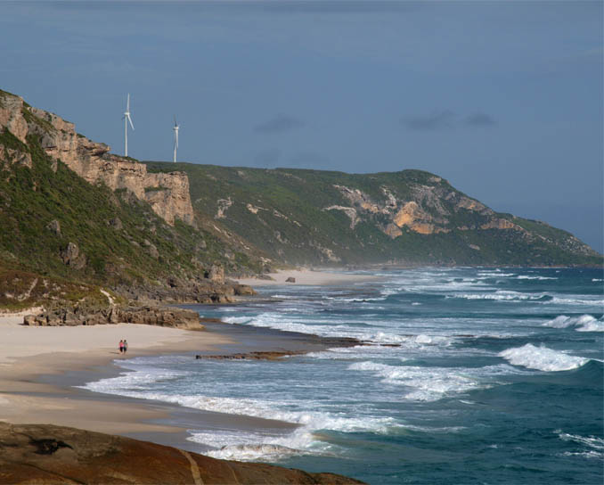A photo of the turbines as seen from Lights Beach, approximately 3.5 kilometres West of the site, showing the cliffs that speed up the wind as it hits the turbines.